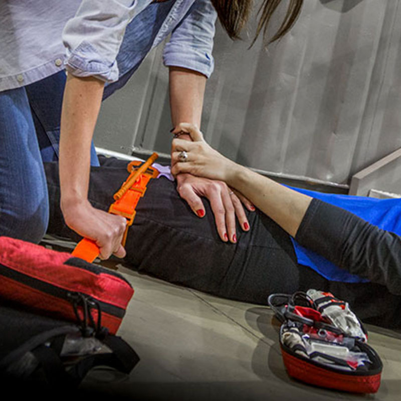 Woman using tourniquet on victims leg to stop the bleed of a wound.